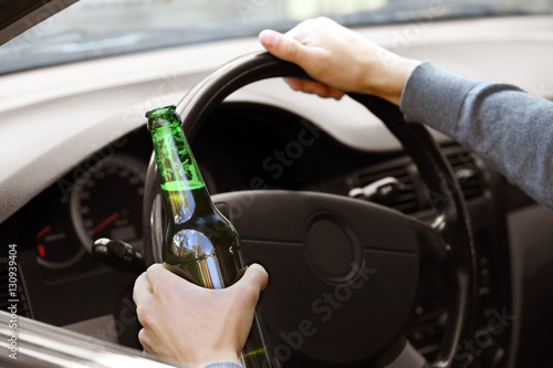 Man holding bottle of beer while driving car, closeup. Don't drink and drive concept