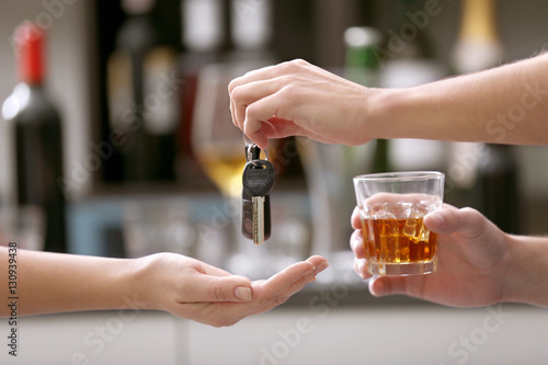 Drunk man giving car key to woman, on blurred background. Don't drink and drive concept