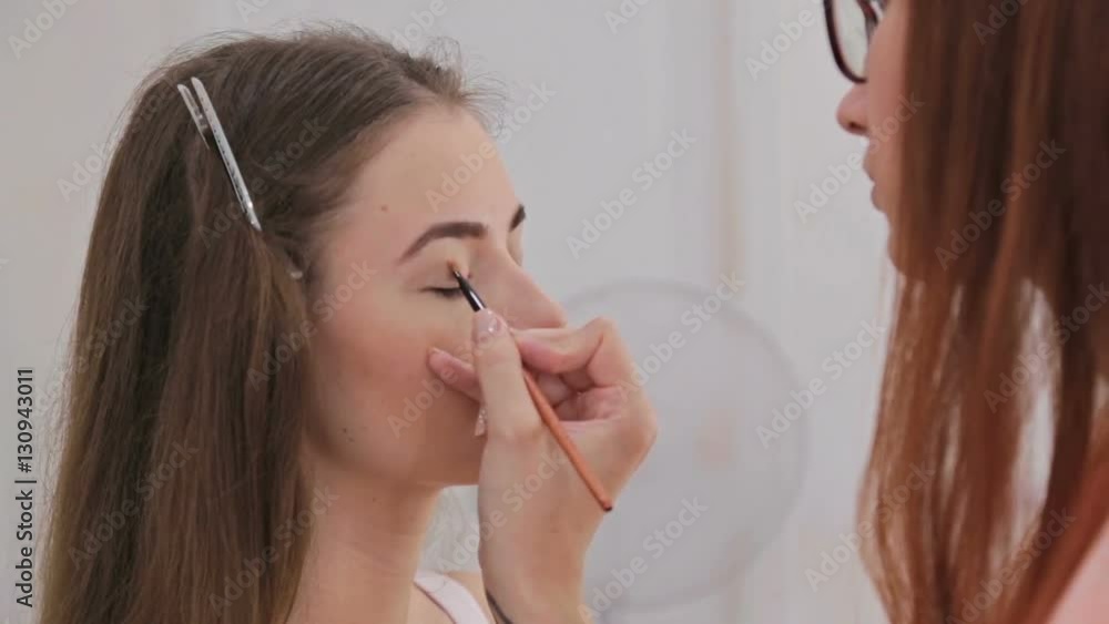 Professional make-up artist applies eye shadow to eyelid of model in white room. Beauty, makeup and fashion concept Professional make-up artist applies eye shadow to eyelid of model in white room. Beauty, makeup and fashion concept