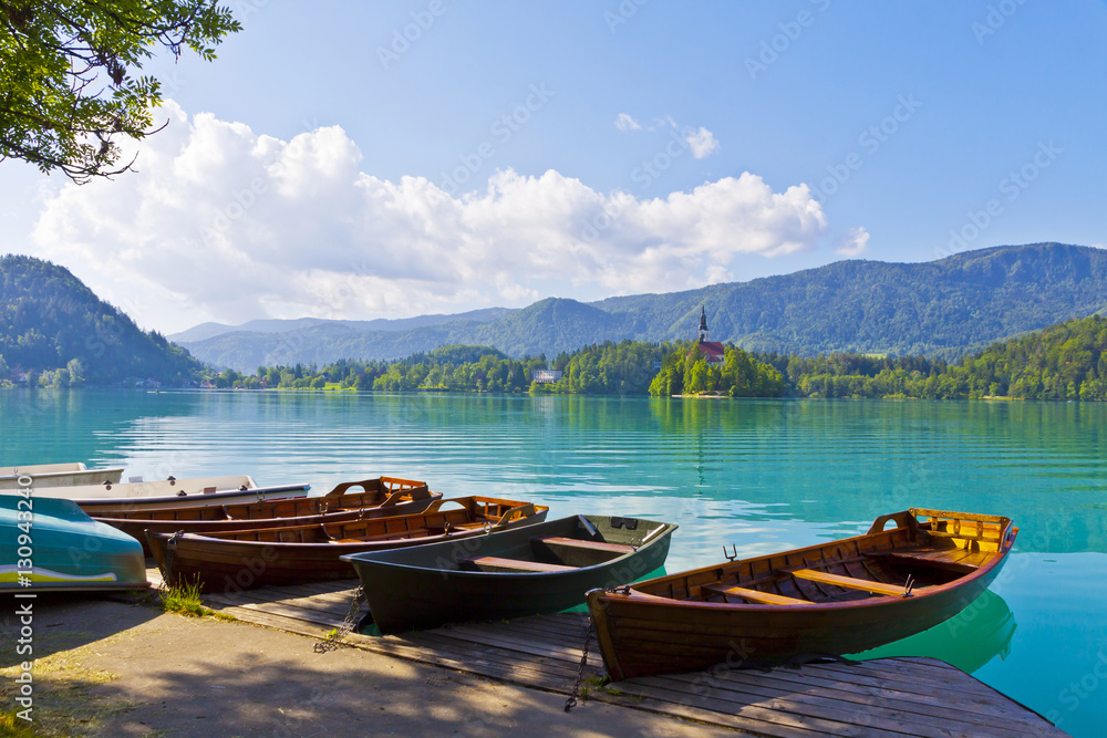 Landscape with boats at the pier of Bled Lake, Bled, Slovenia. Assumption of Mary Church (Cerkev Marijinega vnebovzetja) on the Bled island on the background