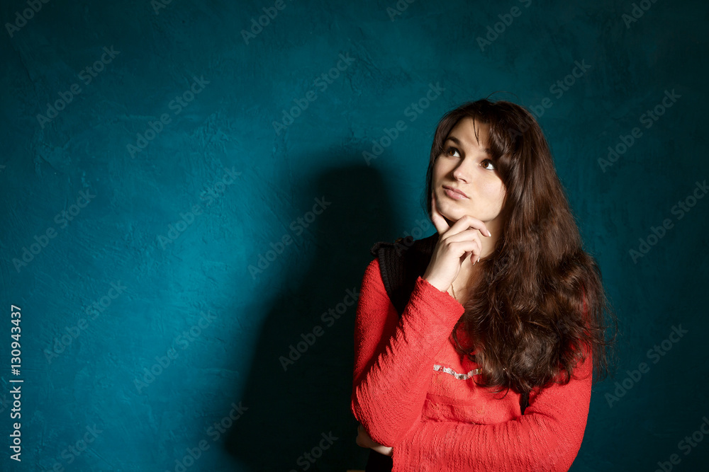 young brunette woman in a beauty blouse and black jacket standing against the backdrop of a blue wall and thinks young brunette woman in a beauty blouse and black jacket standing against the backdrop of a blue wall and thinks