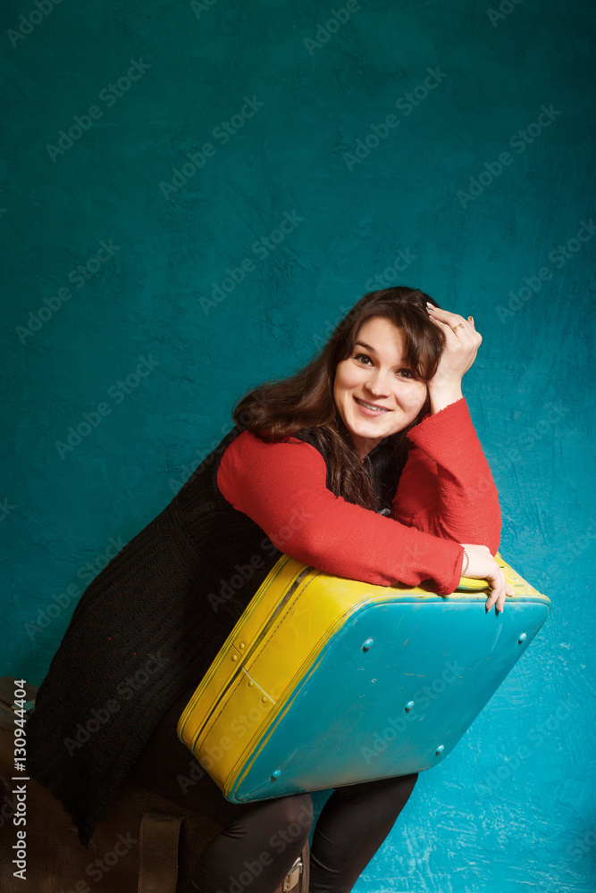 young brunette woman holding a big old suitcase against the backdrop of a blue wall