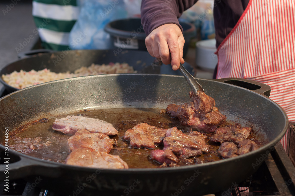Man prepares fried meat in a pan at Christmas market Man prepares fried meat in a pan at Christmas market