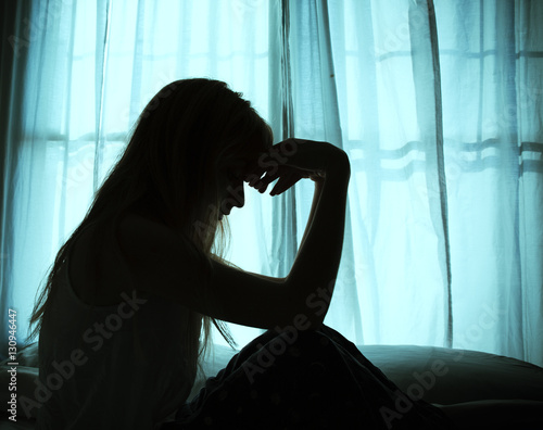 Silhouette of woman sitting in bed by window