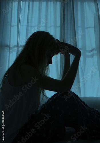 Silhouette of woman sitting in bed by window