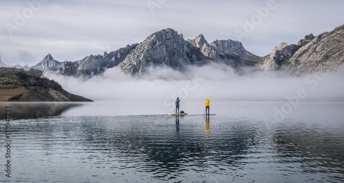 A group of people paddle surfing on a lake with fog and mountains © Dani