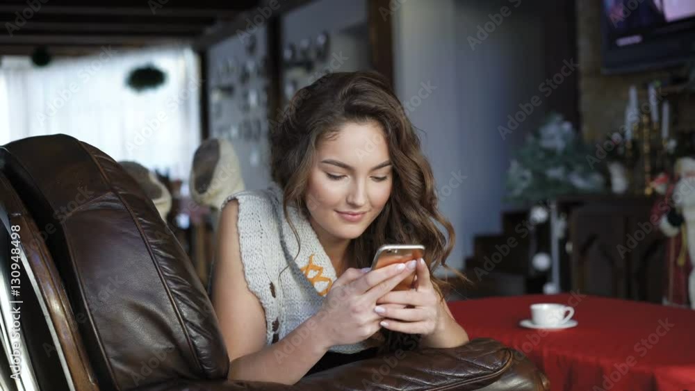 Pretty girl relaxing on the leather sofa and using mobile phone 4K