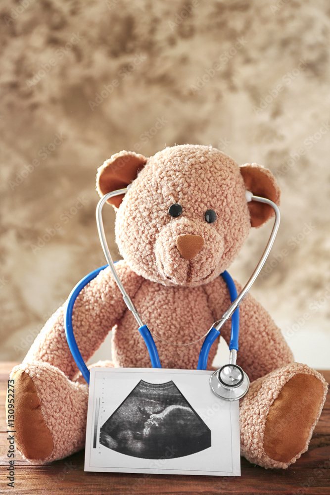 Teddy bear with ultrasound scan of baby and stethoscope on wooden table