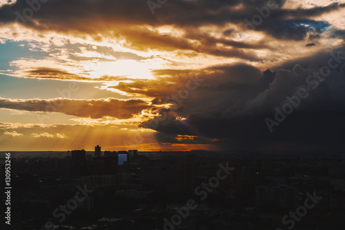 Dramatic yellow and orange scenery of the city silhouette at sunset after storm with massive cloud front and sun god rays