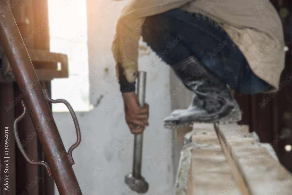 Worker wearing blue jeans and boots, holding a hammer on the scaffold,in construction site (focus at bar steel )