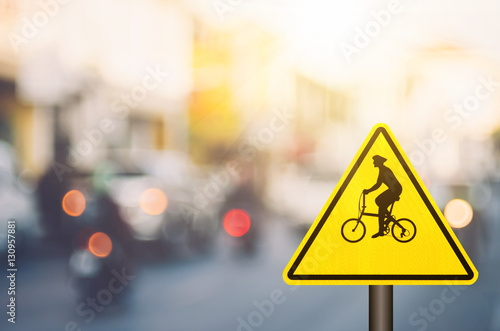 Bicycle warning sign on blur traffic road with colorful bokeh light abstract background.