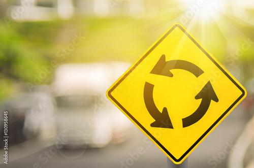Принти на полотні Roundabout warning sign on blur traffic road with colorful bokeh light abstract background