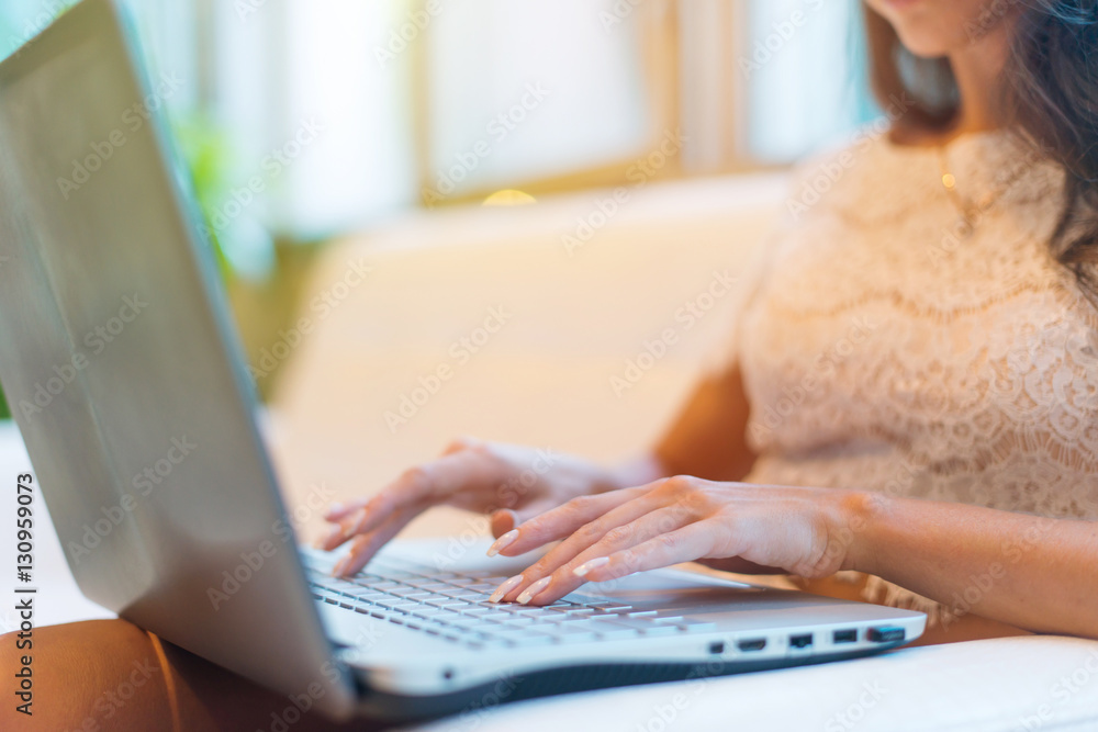 Fototapeta premium Female hands typing on keyboard. Cropped photo of a young woman holding laptop her knees and working.