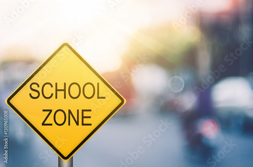 School zone warning sign on blur traffic road with colorful bokeh light abstract background.