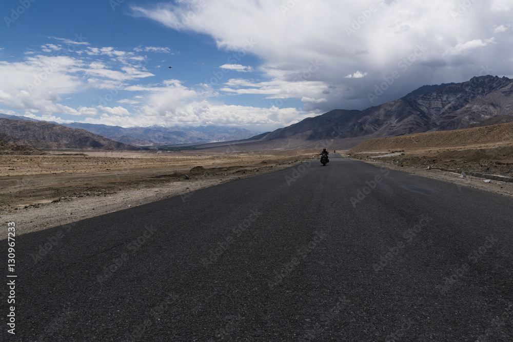 Motorcycle moving on a straight road in desert plains of Ladakh, with Himalayan mountains in the background. Ladakh is a cold desert in Tibetan plateau.