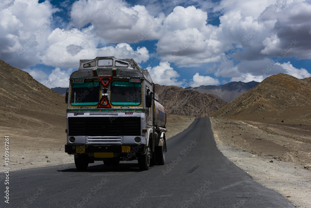 Truck moving on a straight road in desert plains of Ladakh, with Himalayan mountains in the background. Ladakh is a cold desert in Tibetan plateau. Truck moving on a straight road in desert plains of Ladakh, with Himalayan mountains in the background. Ladakh is a cold desert in Tibetan plateau.