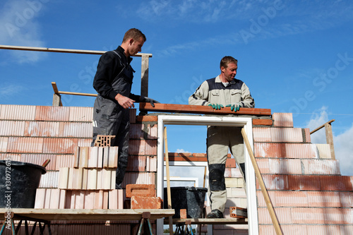 Masons bricklayers putting a lintel as a team together outdoors