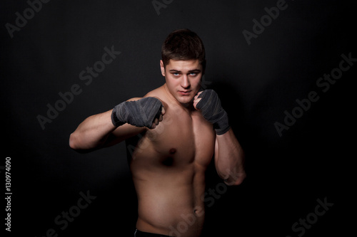 Muscular athletic man boxing on a black background. A man with a naked torso in shorts, hands peremotanye bandages for boxing. © nazarets