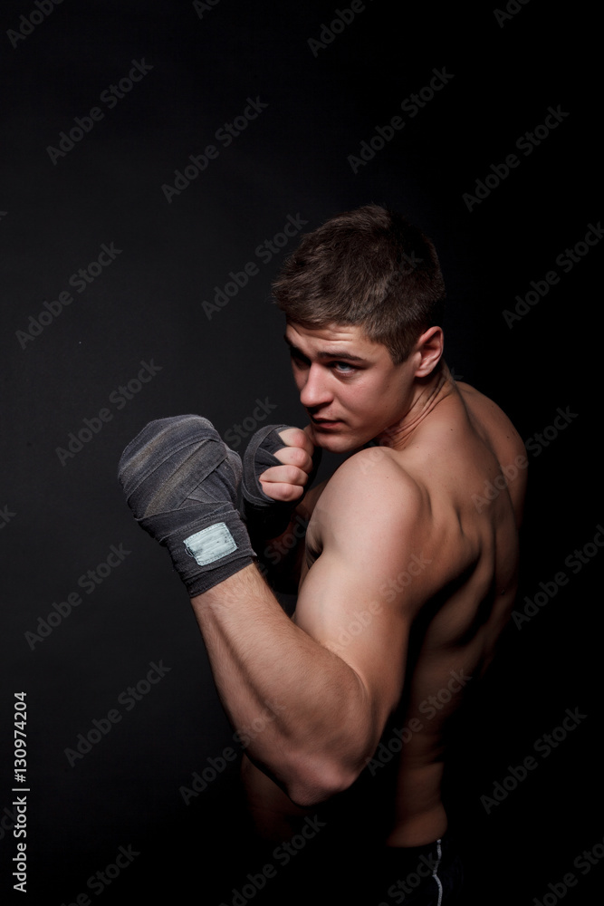 Muscular athletic man boxing on a black background. A man with a naked torso in shorts, hands peremotanye bandages for boxing.