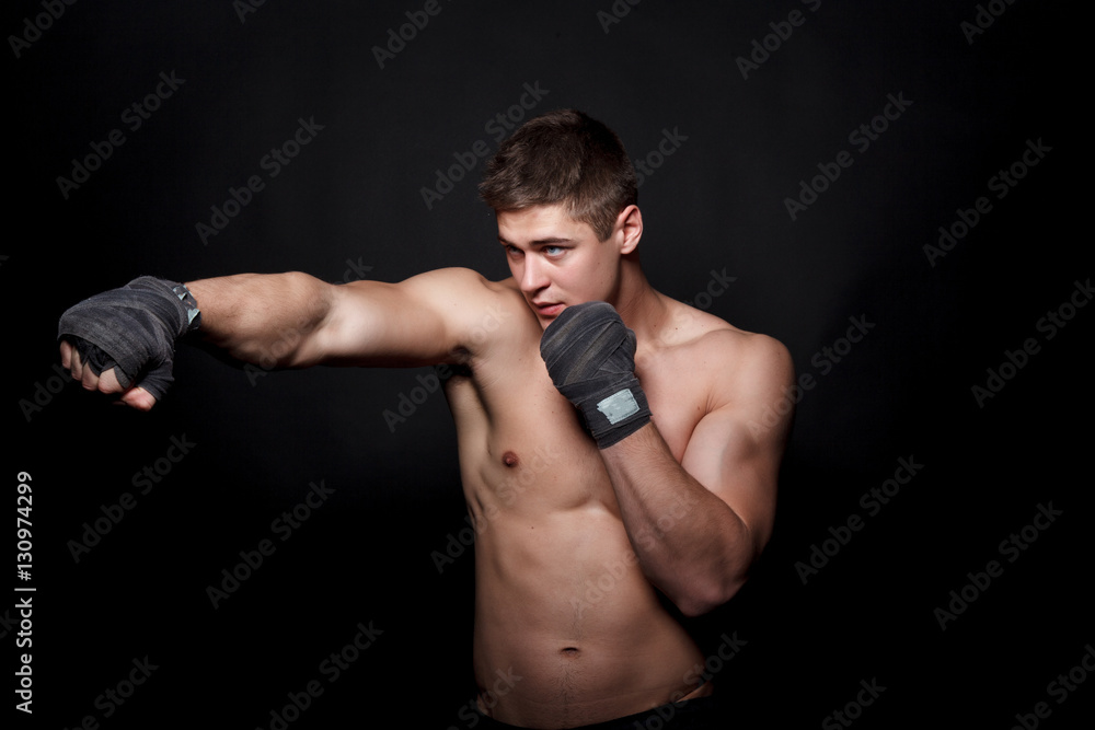 Muscular athletic man boxing on a black background. A man with a naked torso in shorts, hands peremotanye bandages for boxing.