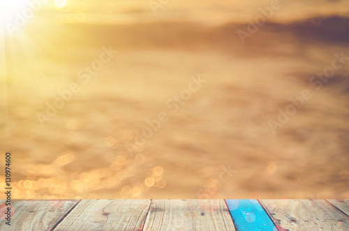 Blur beautiful tropical sunset beach with bokeh sun light wave on copy space empty old wood table abstract background.