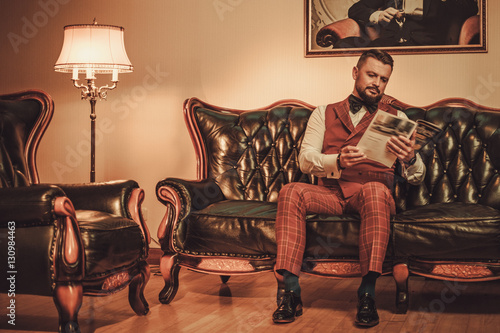 Extravagant stylish man sitting on classic leather sofa in gentleman club photo