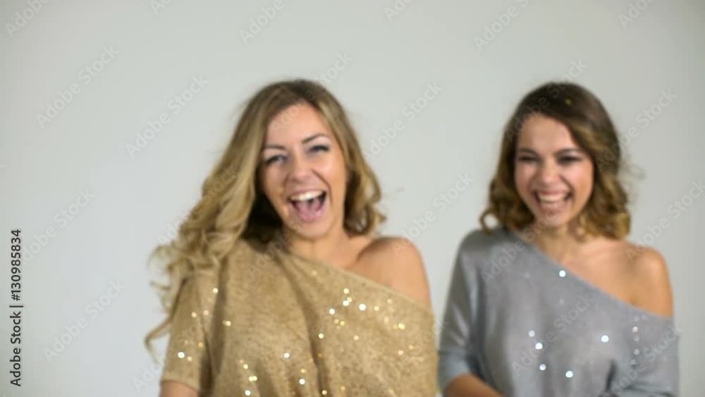 Two beautiful girls in shiny blouses throw confetti on a white background