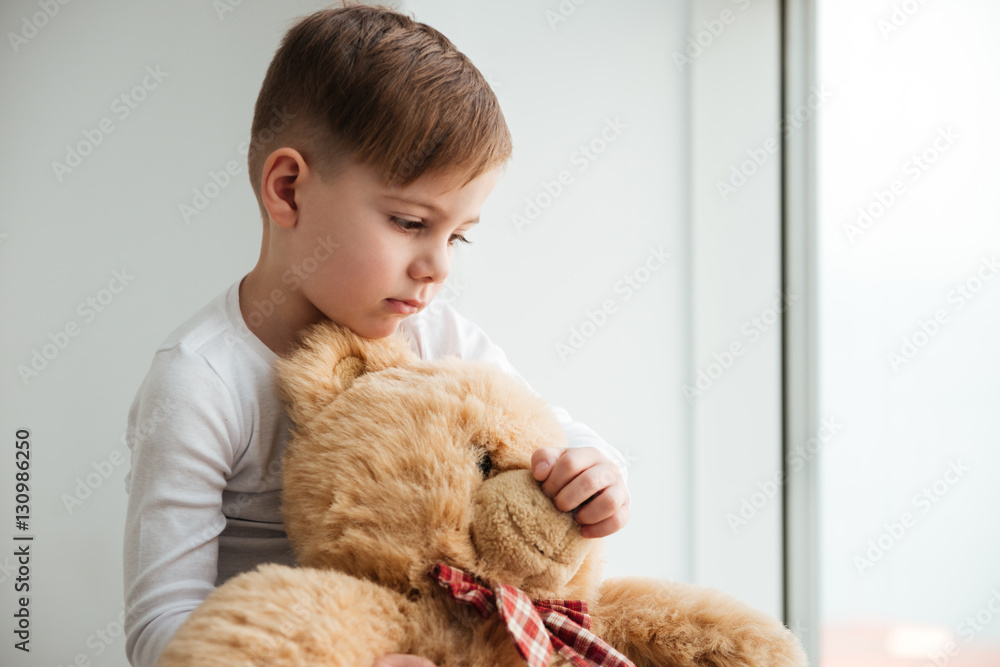 Sad boy near window with teddy bear waiting for parents Sad boy near window with teddy bear waiting for parents