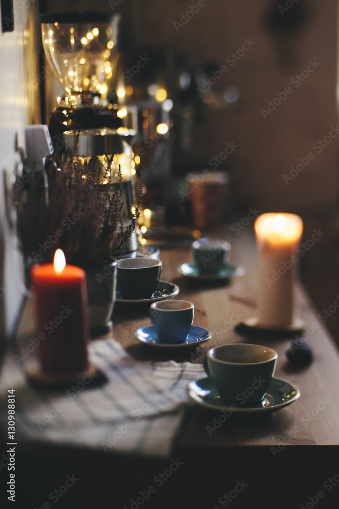 Beautiful festive evening table served. On the wooden table: colorful coffee cups with saucers,napkin, burning candles and some christmas fireflies