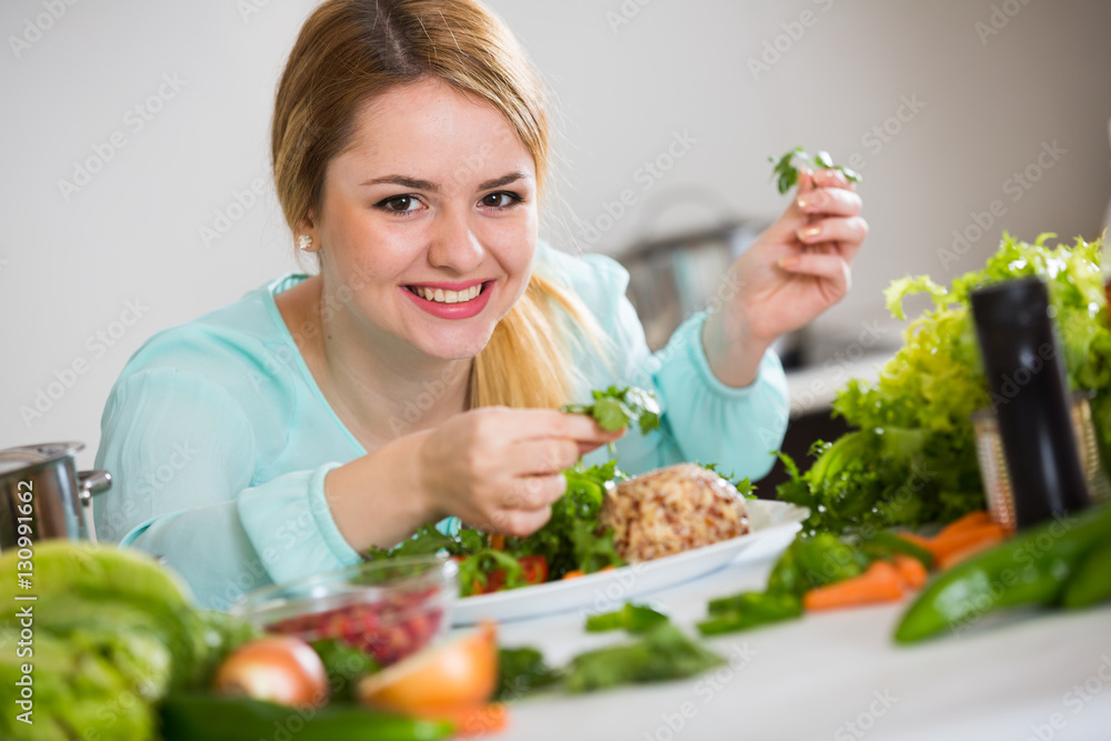 Positive housewife with plate of salad in kitchen