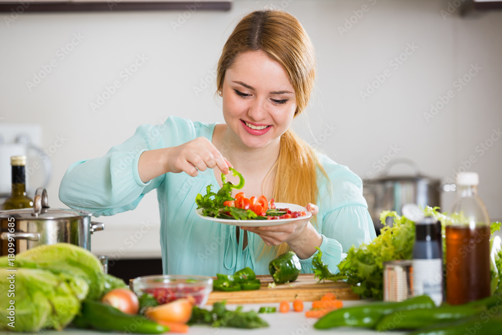 Young woman decorating salad with herbs in kitchen