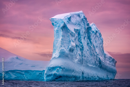 Antarctic iceberg in the snow floating in open ocean. Pink sunset sky in the background. Beauty world