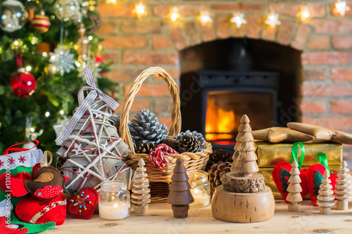 Diy Christmas: wooden toys, felt decorations, presents on the table, Christmas tree and fireplace with burning fire on the background, selective focus photo