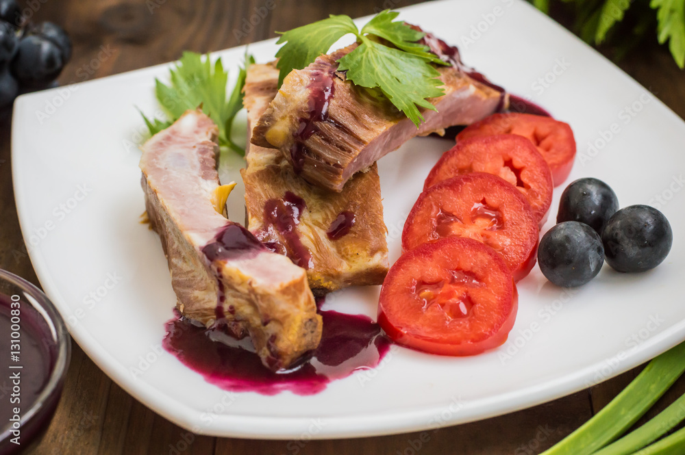 Smoked pork ribs with grape sauce, herbs and vegetables. Wooden background. Top view. Close-up Smoked pork ribs with grape sauce, herbs and vegetables. Wooden background. Top view. Close-up