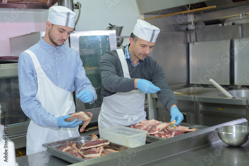 apprentice and chief preparing meat in restaurant kitchen