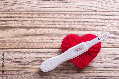 Pregnancy test positive with two stripes, close red woolen heart