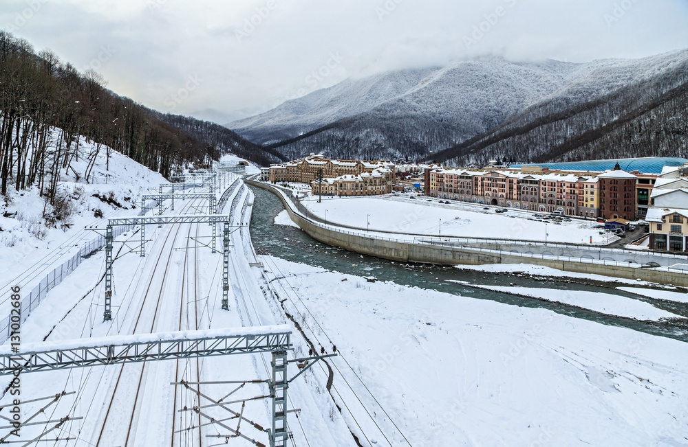Snowy winter scenic landscape of a mountain ski resort featuring a mountain river and railway tracks