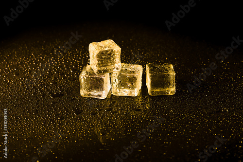 Ice cubes in yellow light on black wet table.