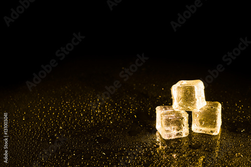 Fototapeta Naklejka Na Ścianę i Meble -  Ice cubes in yellow light on black wet table.