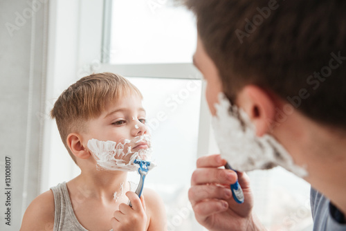 Father and son shaving in bathroom looking at each other photo