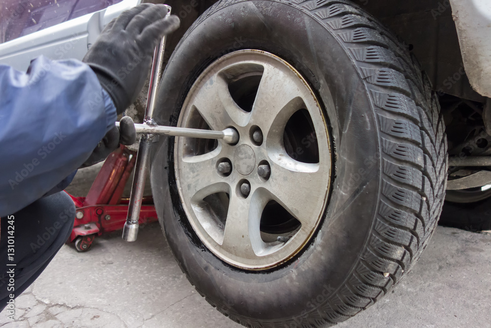 Professional car mechanic changing car wheel with a wrench Professional car mechanic changing car wheel with a wrench