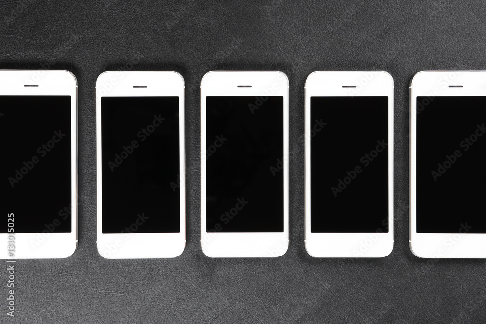 White smartphones lying in a row on dark surface White smartphones lying in a row on dark surface