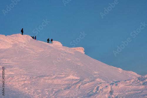 The people on the top of the snow-capped mountain lit by evening sun rays. This photo was taken in Kirovsk in Khibiny mountains, Murmansk Region, Russia.