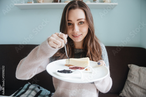 Cute woman sitting in cafe and having breakfast with cake