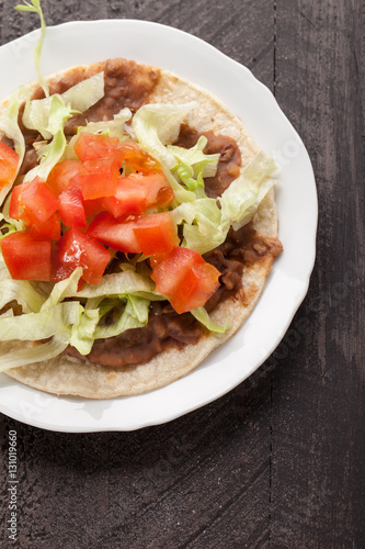 Corn tortilla tostada with refried beans, lettuce, salsa, and tomatoes top view on a dark wooden background