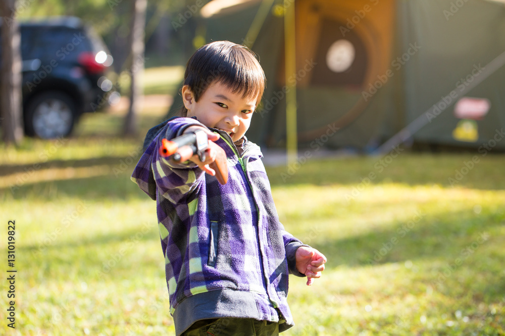Healthy Asian boy playing toy gun smiling cute in morning sun light and green grass at camping site Healthy Asian boy playing toy gun smiling cute in morning sun light and green grass at camping site