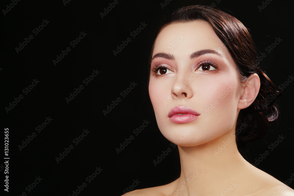 Fototapeta premium Portrait of young beautiful woman with fresh make-up looking upwards over dark background