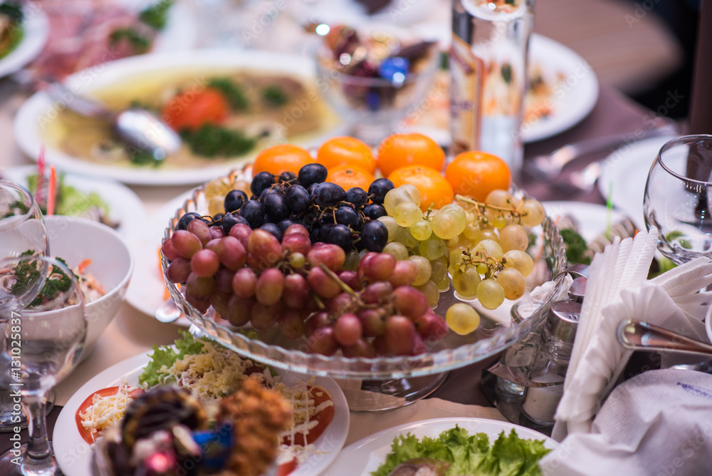 Fruits - Grapes, pears, tangerines. Against the background of the table with appetizers Fruits - Grapes, pears, tangerines. Against the background of the table with appetizers
