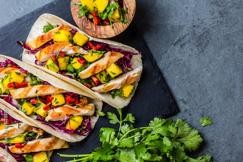 Mexican chicken tacos with vegetables and mango. Slate background