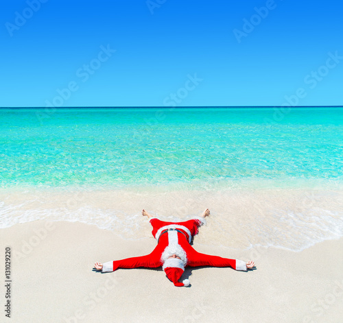 Christmas Santa Claus tanning at tropical ocean beach in waves
